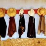 5 jackets and hats hanging on a wall over a wooden bench