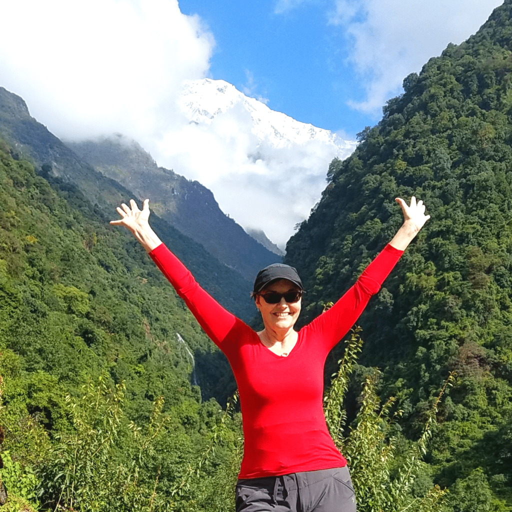 Denise with hands in air in front of Anapurna mountain in Nepal