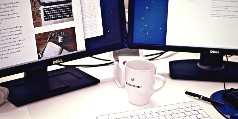 desk with two computer monitors, coffee cup and keyboard